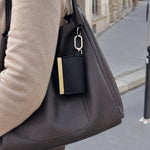 Bijou negro colgado del asa de un bolso, con el mosquetón dorado